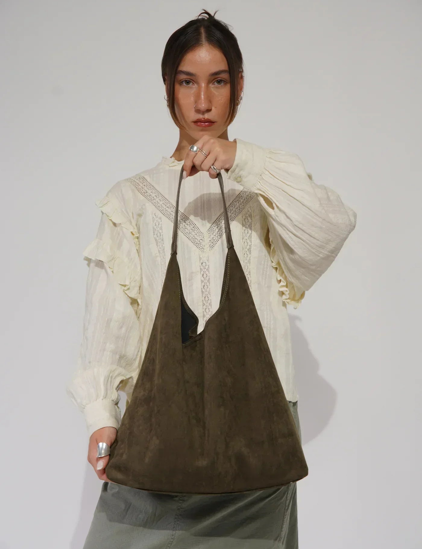 Donna con borsa a spalla in pelle scamosciata marrone, indossa camicia bianca con dettagli in pizzo. Moda donna, accessori eleganti, stile casual.