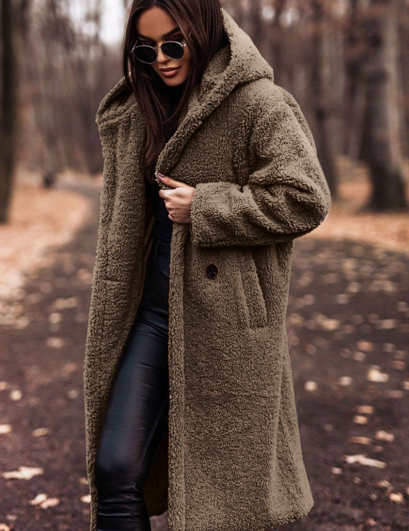 Donna con cappotto teddy marrone, occhiali da sole, pantaloni neri in pelle, in un parco autunnale. Moda invernale, stile casual chic.