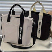 Due borse a tracolla in tessuto, una bianca e una nera, con manici e scritta "EVES CAMIER". Design moderno, ideale per moda casual e shopping.