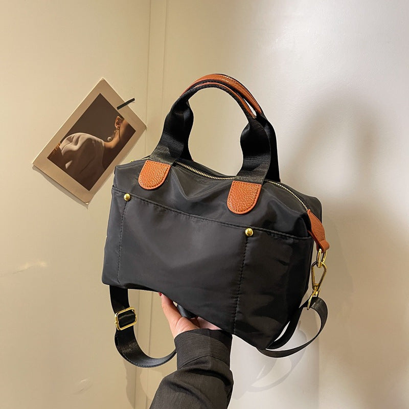 Borsa a mano nera in nylon con dettagli in pelle marrone, tracolla regolabile, design elegante e moderno, perfetta per uso quotidiano.