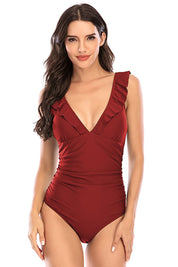 Donna in costume intero rosso con volant, scollo a V profondo. Moda mare elegante, abbigliamento estivo, tendenze costumi da bagno 2023.
