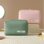 Due astucci per trucco in tessuto, uno verde e uno rosa, su scatole beige. Specchio rotondo sullo sfondo. Accessori cosmetici eleganti e pratici.