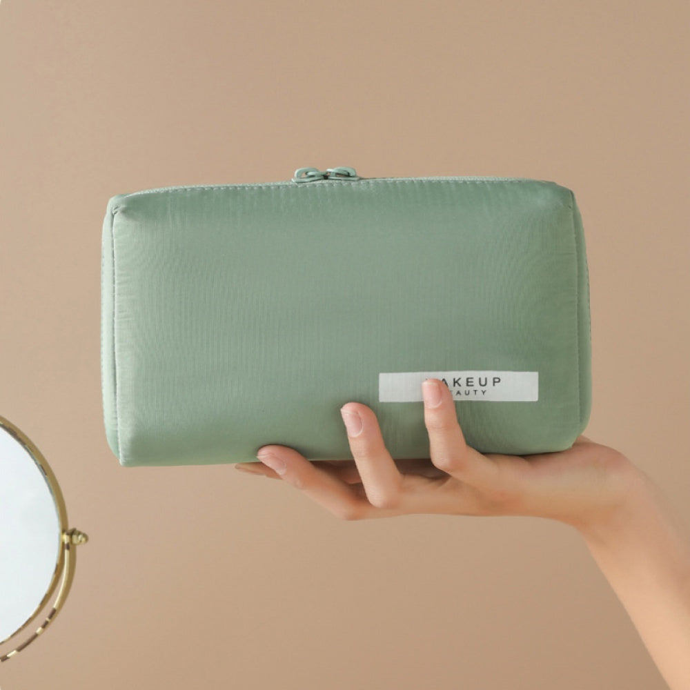 Astuccio verde per trucco, elegante e compatto, tenuto in mano. Ideale per organizzare cosmetici. Accessorio essenziale per beauty routine.