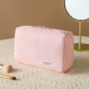 Astuccio trucco rosa su tavolo beige, specchio rotondo, pennelli trucco. Elegante borsa cosmetica, organizer viaggio, accessori bellezza.