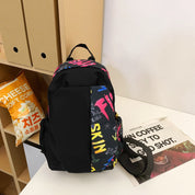 Zaino nero con scritte colorate su scaffale, accanto a sacchetto di popcorn e giornale. Design moderno, ideale per scuola o viaggio.