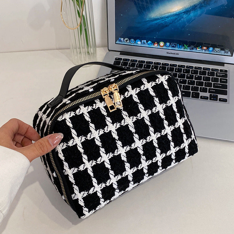 Borsa a mano in tessuto a scacchi bianco e nero con cerniera dorata, posizionata davanti a un MacBook Air su una scrivania moderna.