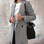 Cappotto grigio elegante da donna, abbinato a maglione bianco con scritta, borsa nera e orologio da polso. Moda autunnale chic.