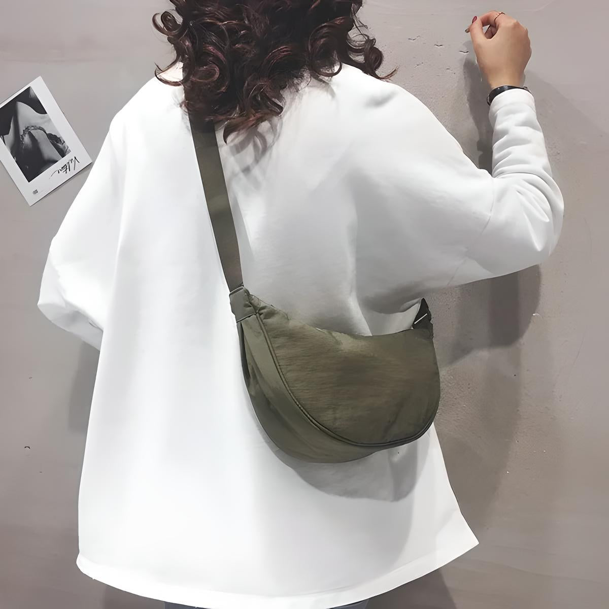 Donna con felpa bianca e borsa a tracolla verde oliva, capelli ricci. Stile casual, moda urbana. Accessori donna, tendenze autunno.