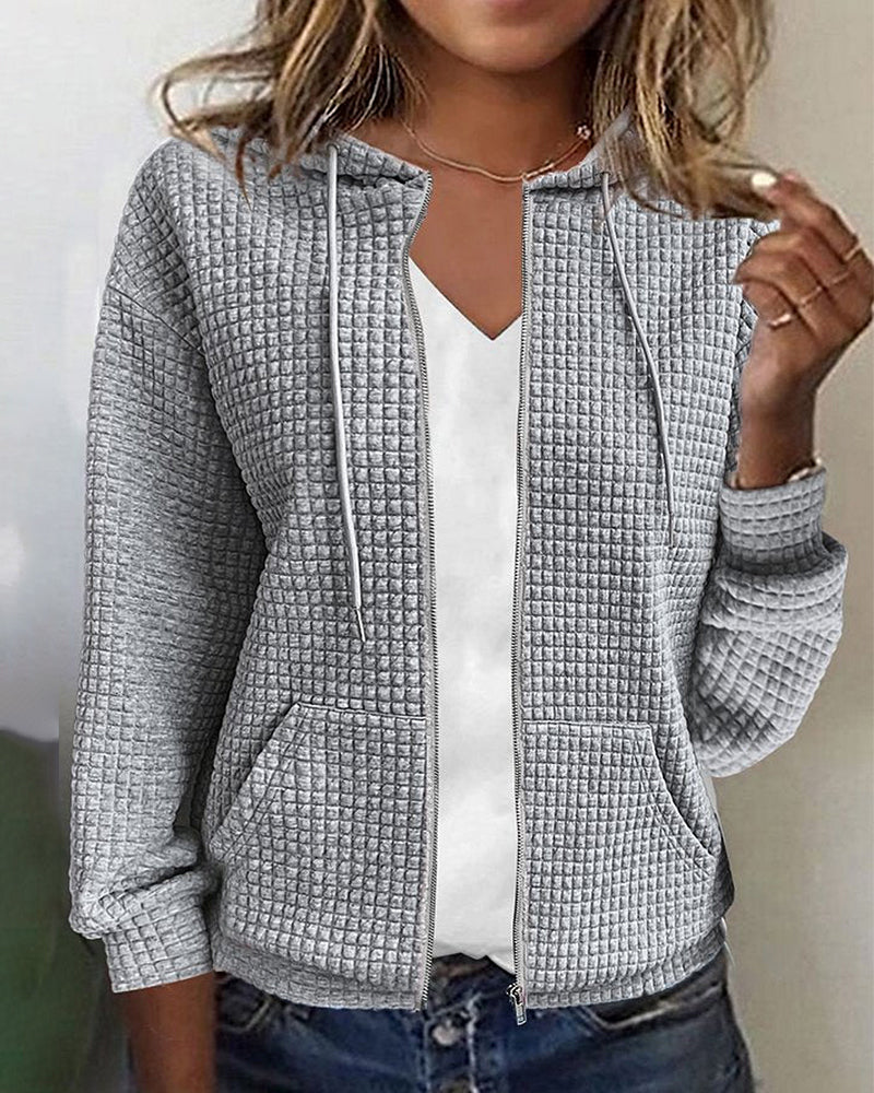 Giacca donna grigia con cappuccio, tessuto a trama waffle, zip frontale, tasche laterali, indossata su maglietta bianca. Moda casual autunnale.