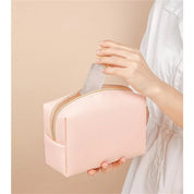 Donna inserisce flacone trasparente in beauty case rosa. Accessori da viaggio, organizzazione cosmetici, borsa trucco elegante.