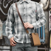 Camicia a quadri grigia e bianca da uomo, abbinata a jeans e borsa a tracolla marrone. Stile casual, moda urbana, abbigliamento maschile.