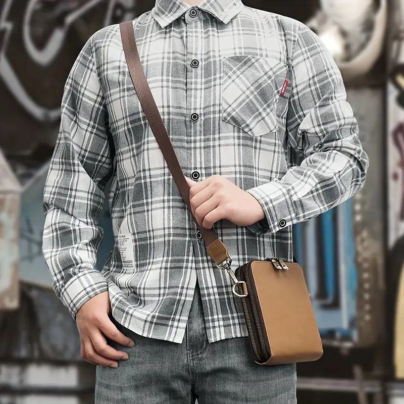 Camicia a quadri grigia e bianca da uomo, abbinata a jeans e borsa a tracolla marrone. Stile casual, moda urbana, abbigliamento maschile.