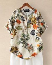 Camicia donna floreale, maniche corte, bottoni, stampa tropicale, colori vivaci, casual, estiva, su gruccia, sfondo beige.