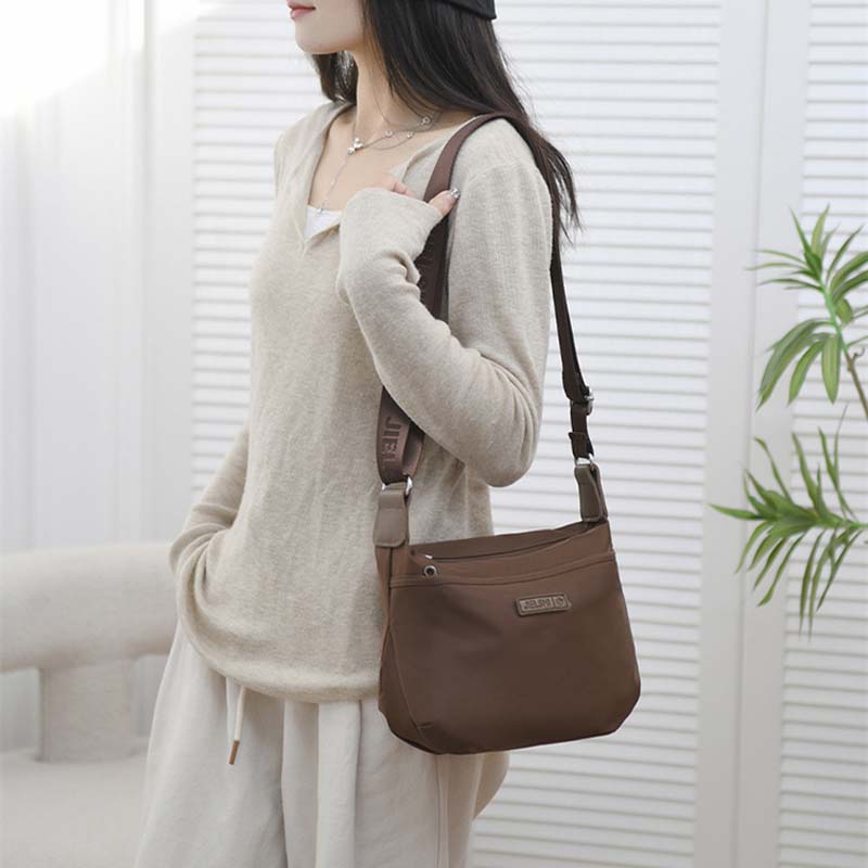 Donna con borsa a tracolla marrone, design casual, indossa maglione beige e pantaloni bianchi. Accessorio moda femminile, stile urbano elegante.