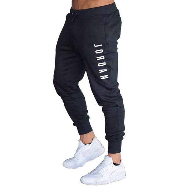 Pantaloni sportivi neri da uomo con scritta "Jordan", abbinati a scarpe da ginnastica bianche. Stile casual, moda streetwear.
