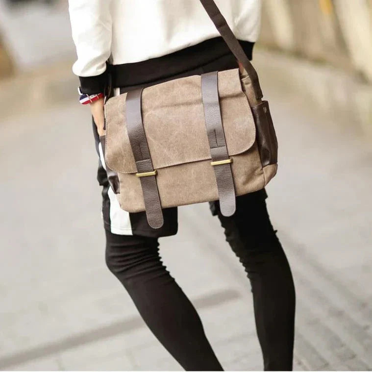 Borsa a tracolla in tela marrone con cinghie in pelle, indossata da una persona in pantaloni neri. Stile casual, ideale per uso quotidiano.
