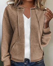 Giacca donna beige con cappuccio, tessuto trapuntato, chiusura zip, tasche frontali, abbinata a maglietta bianca. Moda casual autunnale.