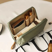 Astuccio da viaggio verde aperto con scomparti, contenente cosmetici e accessori. Organizzatore compatto per trucco, ideale per viaggi.