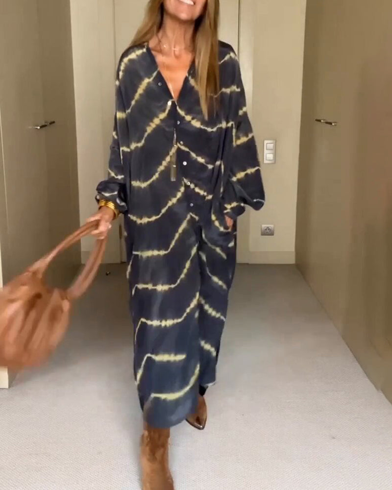 Abito lungo a righe tie-dye blu e gialle, maniche lunghe, indossato con stivali marroni e borsa in pelle. Moda donna casual autunnale.