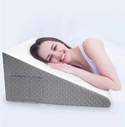 Donna sorridente sdraiata su cuscino a cuneo ortopedico grigio, supporto per schiena e collo, ideale per dormire e relax.