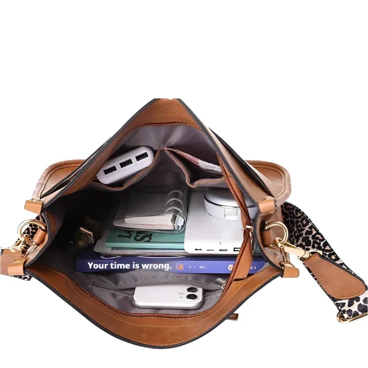 Interno di borsa a tracolla in pelle marrone con libri, smartphone, power bank e taccuino. Cinghia leopardata. Accessori moda donna.