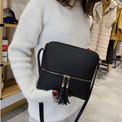 Donna con maglione bianco tiene borsa a tracolla nera in pelle con cerniera e nappe. Moda autunno, accessori eleganti, negozio abbigliamento.