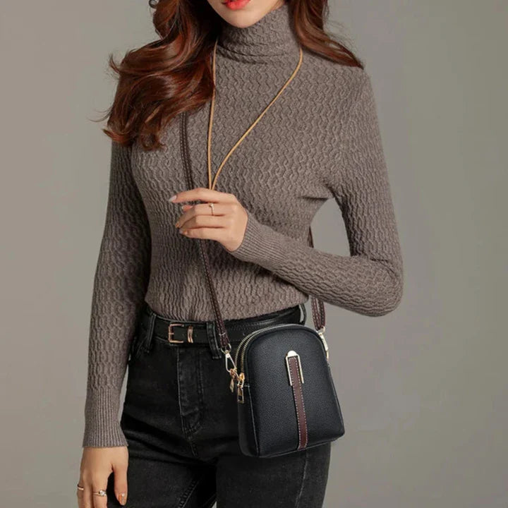 Donna con maglione a collo alto marrone, jeans neri e borsa a tracolla nera. Moda autunnale, abbigliamento casual elegante.
