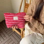 Donna con maglione beige tiene una borsa a righe rosse e rosa in maglia, etichetta "bookish beauty", seduta su sedia di legno. Accessorio moda trendy.