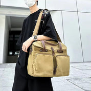 Uomo con borsa a tracolla in tela beige, tasche frontali, abbigliamento casual nero, orologio digitale, esterno urbano.