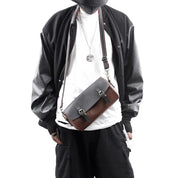 Uomo con giacca nera e borsa a tracolla in pelle bicolore, stile casual urbano. Accessorio moda maschile, tendenza streetwear.