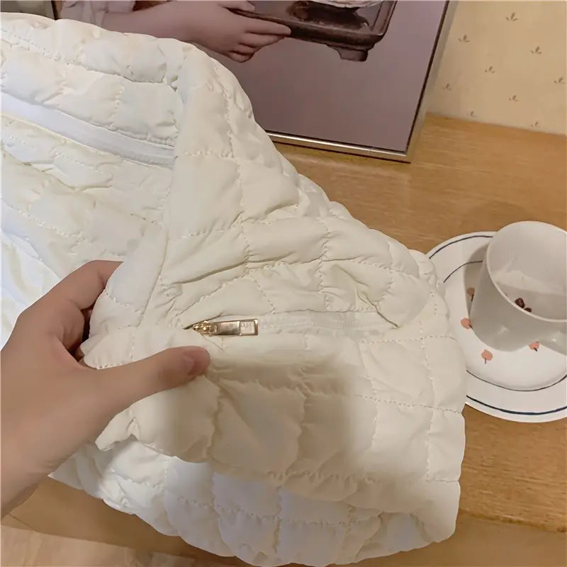 Giacca trapuntata bianca con cerniera dorata su tavolo di legno, accanto a tazza di tè e quadro. Tessuto invernale caldo e alla moda.