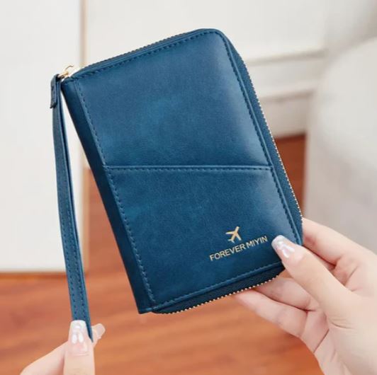 Portafoglio da viaggio blu in pelle con cerniera, logo "Forever Mivin", tenuto in mano. Accessorio elegante e pratico per documenti e carte.