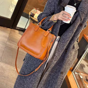 Cappotto grigio elegante, borsa a tracolla in pelle marrone, donna con caffè da asporto. Moda autunnale, accessori di tendenza.