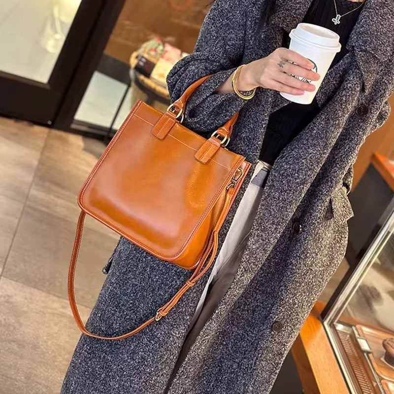Cappotto grigio elegante, borsa a tracolla in pelle marrone, donna con caffè da asporto. Moda autunnale, accessori di tendenza.