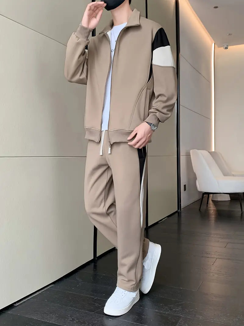 Uomo in tuta sportiva beige con dettagli neri e bianchi, indossa scarpe da ginnastica bianche. Stile casual, moda maschile, abbigliamento sportivo.