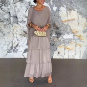 Abito lungo elegante grigio con balze, accessoriato con collana e pochette dorata. Moda donna, abbigliamento chic, outfit serale sofisticato.