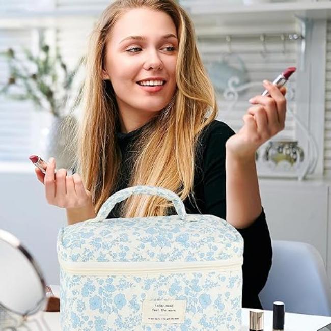 Giovane donna sorridente con rossetto rosso, borsa trucco floreale blu in primo piano. Ambiente luminoso, prodotti cosmetici.