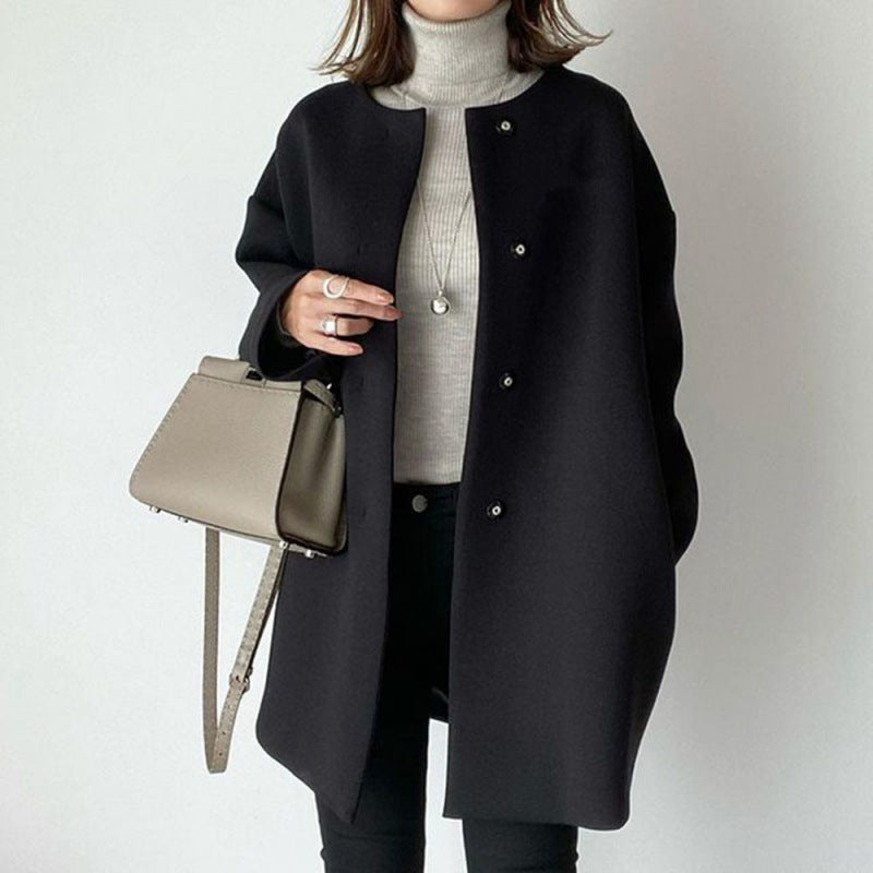 Cappotto nero elegante donna, abbinato a maglione grigio e borsa a tracolla beige. Moda autunnale, stile minimalista, abbigliamento casual chic.