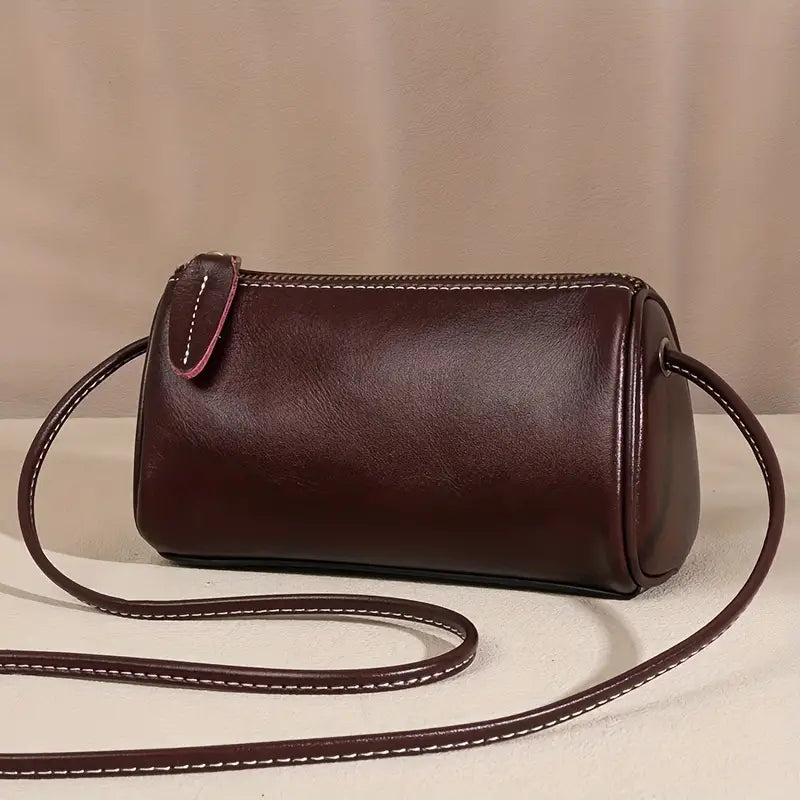 Borsa a tracolla cilindrica in pelle marrone scuro, design elegante, cuciture bianche a contrasto, accessorio moda donna, stile minimalista.