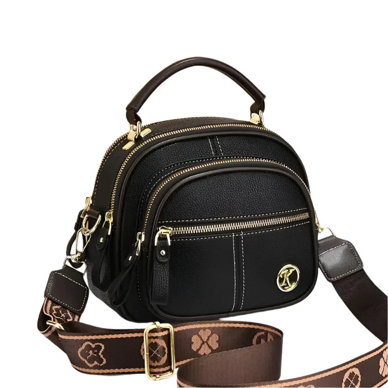 Borsa a tracolla nera in pelle con dettagli dorati, manico superiore, cerniere multiple e tracolla regolabile marrone con motivo floreale.