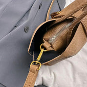 Borsa in pelle marrone con cerniera dorata su giacca grigia. Accessorio moda elegante, perfetto per look autunnali.