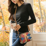 Donna con borsa a tracolla multicolore in pelle, maglia nera e jeans, tiene una tazza di caffè. Moda autunnale casual.