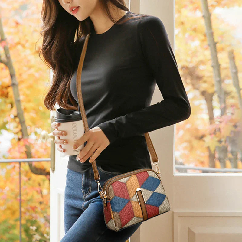Donna con borsa a tracolla multicolore in pelle, maglia nera e jeans, tiene una tazza di caffè. Moda autunnale casual.