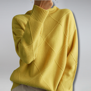 Maglione giallo a rombi, tessuto a maglia, maniche lunghe, stile casual, moda autunno inverno, abbigliamento donna, sfondo grigio chiaro.