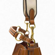 Borsa a secchiello in pelle marrone con tracolla regolabile in tessuto beige, dettagli in metallo dorato, design elegante e moderno.