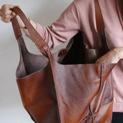 Borsa shopper in pelle marrone, ampia e resistente, indossata da una persona in maglia rosa. Design elegante, ideale per shopping e uso quotidiano.