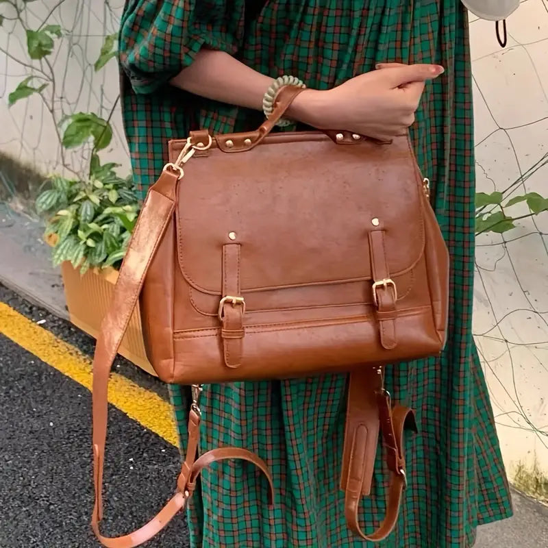 Borsa a tracolla in pelle marrone con fibbie dorate, indossata da una persona in abito a quadri verdi. Accessorio moda elegante e versatile.