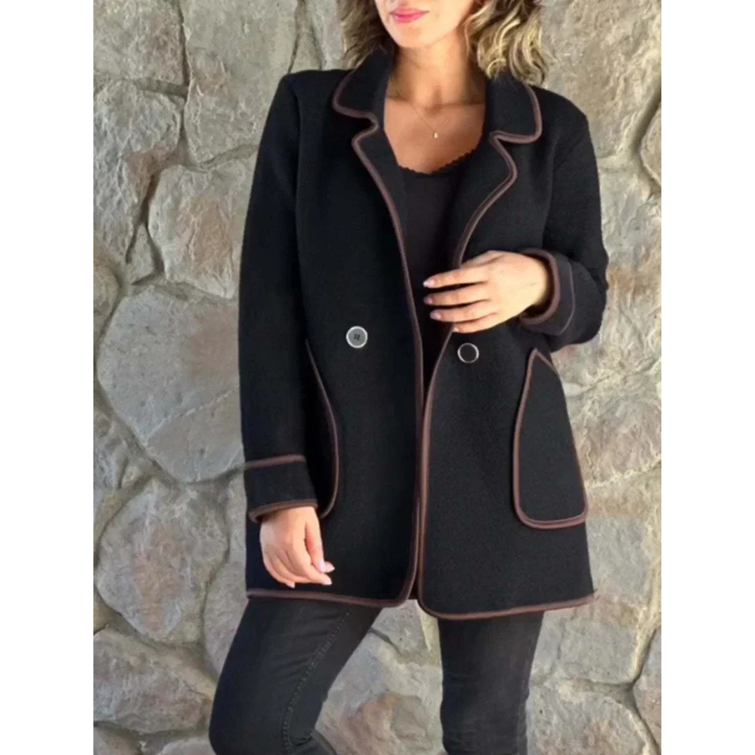 Cappotto donna nero elegante con bordi marroni, doppio petto, su sfondo di pietra. Moda autunno inverno, abbigliamento femminile chic.