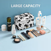 Borsa trucco grande capacità bianca e nera, design mucca, con prodotti cosmetici vari, pennelli, creme e profumi su sfondo blu.