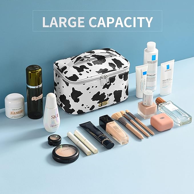 Borsa trucco grande capacità bianca e nera, design mucca, con prodotti cosmetici vari, pennelli, creme e profumi su sfondo blu.
